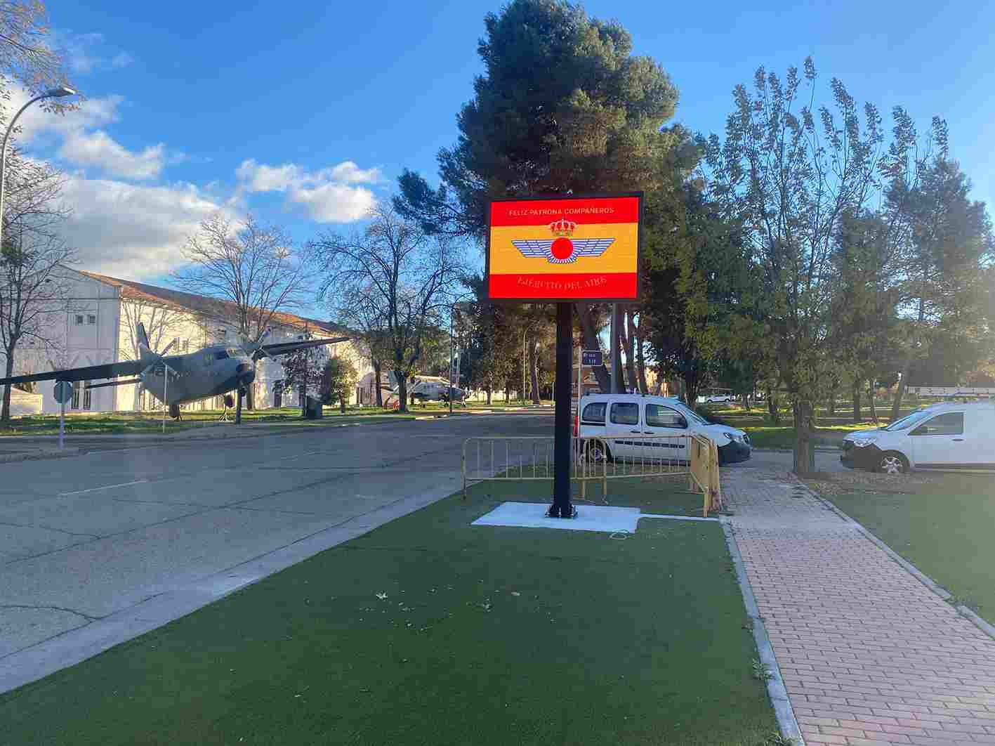 Monoposte LED exterior mostrando la bandera de España en una zona ajardinada con árboles