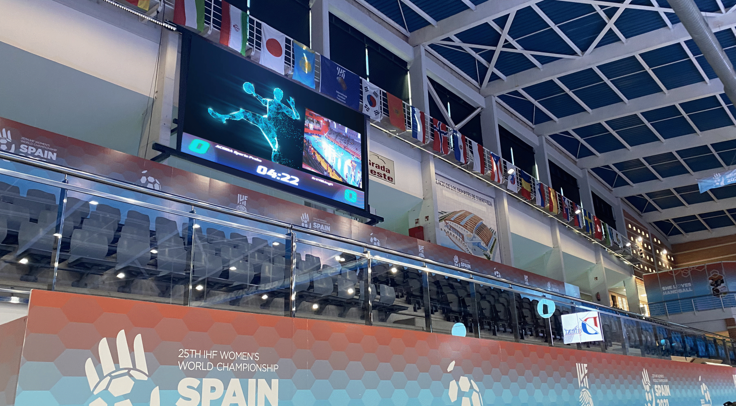 Interior de pabellón deportivo con banderas de países. Gran pantalla LED muestra gráfico de baloncesto.