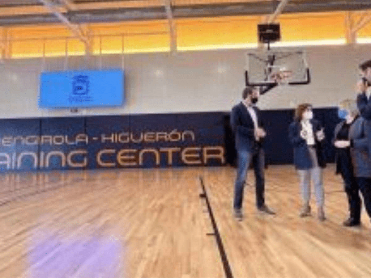 Cancha de baloncesto interior, gran cartel de entrenamiento y dos personas con mascarilla.