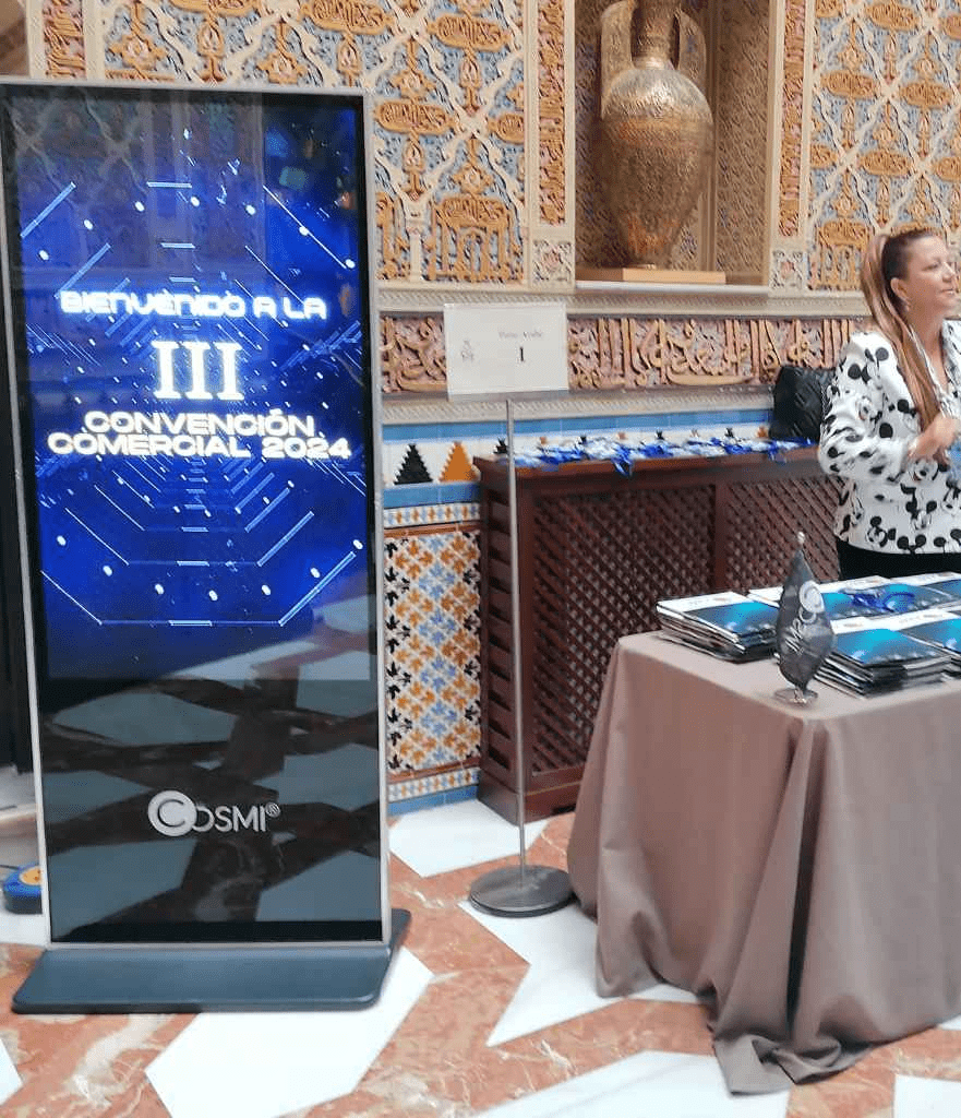 Mupi digital de Cosmi anunciando la III Convención Comercial 2026 en un salón de eventos.
